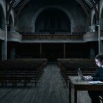 A student working alone on a laptop in a large darkened school hall, representing AI in education without national strategy